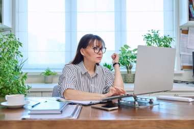 Merkez ofisteki bilgisayar bilgisayarında çalışan orta yaşlı ciddi bir kadın. Olgun bir kadın masada oturuyor, yazı yazıyor ve monitöre bakıyor. Uzak iş, öğretim, iş, blog, serbest