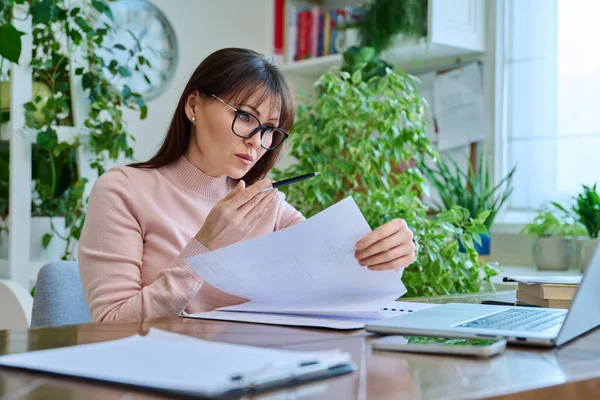 Merkez ofisteki bilgisayar bilgisayarında çalışan orta yaşlı ciddi bir kadın. Masada oturmuş monitörlere, iş belgelerine bakan olgun bir kadın. Uzak iş, öğretim, iş, blog, serbest