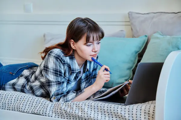 自宅で勉強する大学生の少女は ラップトップとソファーに横たわり 勉強本にノートを作りました トレーニング テクノロジー 若者のコンセプト — ストック写真