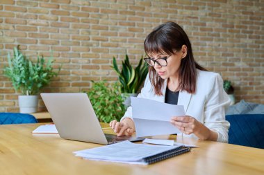Ofisinde dizüstü bilgisayar kağıtlarıyla masasında çalışan olgun, ciddi bir iş kadını. İş, iş, iş, yönetim, finans, hukuk, lojistik, satış, hizmet kavramı