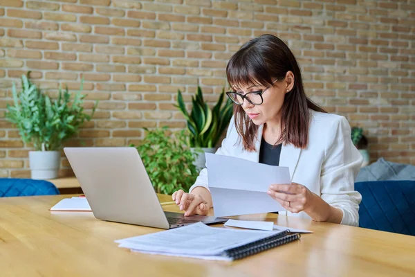 Ofisinde dizüstü bilgisayar kağıtlarıyla masasında çalışan olgun, ciddi bir iş kadını. İş, iş, iş, yönetim, finans, hukuk, lojistik, satış, hizmet kavramı