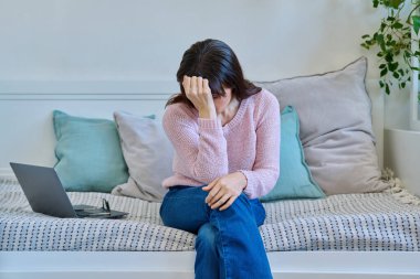 Mutsuz, olgun bir kadının baş ağrısı, stres bunalımı yaşaması evdeki kanepe yatağında oturması. Sağlık ve ruh hali sorunları, yaşla ilgili sorunlar, orta yaşlı kadınlar