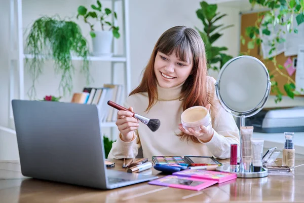 若い女性がノートパソコンのウェブカメラに化粧品を見せ 自宅でテーブルに座った 美容ブログVoog オンラインコース 装飾化粧品の専門的な使用に関するウェビナーをトレーニング — ストック写真