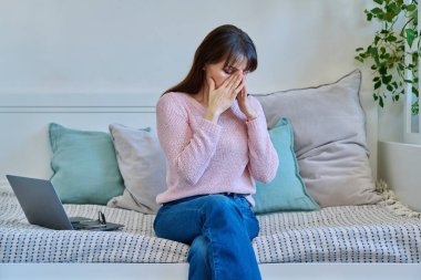 Mutsuz, olgun bir kadının baş ağrısı, stres bunalımı yaşaması evdeki kanepe yatağında oturması. Sağlık ve ruh hali sorunları, yaşla ilgili sorunlar, orta yaşlı kadınlar