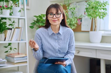 Ofiste dijital tabletle oturmuş kameraya bakan kadın psikolog sosyal hizmet uzmanı portresi. Psikoloji psikoterapisi yardımcı oluyor.