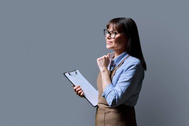 Orta yaşlı, kendine güvenen bir işkadını sahibi, önlüklü bir işçi, gri stüdyo arka plan fotokopi alanında profil görüntüsü. Emirler, çalışma belgeleri, meslek, personel yönetimi kavramı