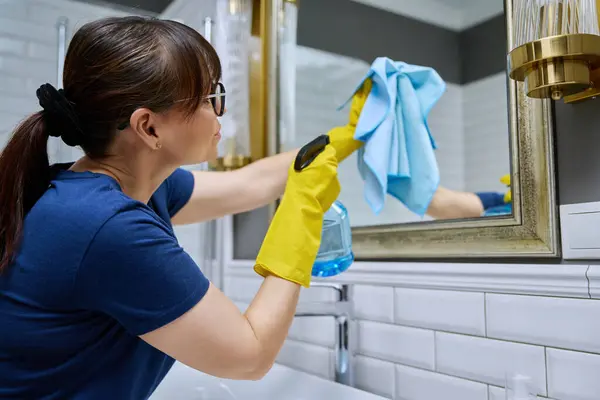 妇女清洁浴室 用喷雾器清洗镜子 用专业的抹布擦拭没有条纹的玻璃 持家家政清洁服务概念 — 图库照片