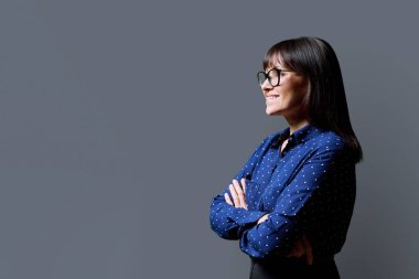 İleri bakan orta yaşlı bir kadının profil görüntüsü, gri stüdyo arka planı, reklam metni için kopya alanı. Olgun iş, kendine güvenen başarılı kadın. Pazarlama satış hizmetleri, insanlar