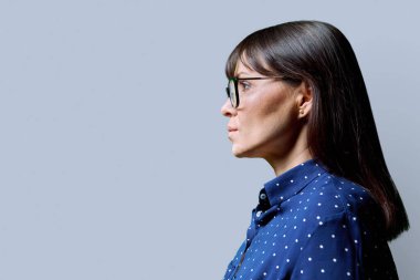 Orta yaşlı, ileriye bakan ciddi bir kadının profil görüntüsü, gri stüdyo arka planı, reklam metni için kopya alanı. Olgun iş, kendine güvenen başarılı kadın. Pazarlama satış hizmetleri, insanlar