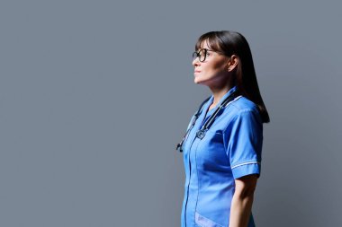 Orta yaşlı, kendine güvenen kadın hemşirenin portresi gri stüdyo arka planında, fotokopi odasında. Tıbbi hizmetler, sağlık, mesleki yardım, tıbbi bakım kavramı