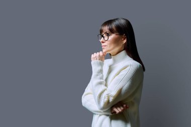 Orta yaşlı, ileriye bakan ciddi bir kadının profil görüntüsü, gri stüdyo arka planı, reklam metni için kopya alanı. Olgun iş, kendine güvenen başarılı kadın. Pazarlama satış hizmetleri, insanlar