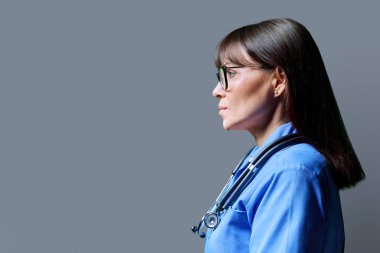 Ciddi orta yaşlı, kendine güvenen kadın hemşirenin portresi gri stüdyo arka planında, fotokopi alanında. Tıbbi hizmetler, sağlık, mesleki yardım, tıbbi bakım kavramı