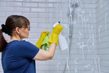 Banyoyu temizleyen kadın, duşta bardağı yıkayan kadın deterjan spreyi ve profesyonel bez parçasıyla. Oda servisi, ev işi, ev temizliği, temizlik hizmeti konsepti.