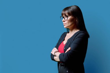 Mavi stüdyo geçmişinde olgun, kendine güvenen ciddi bir kadının profil portresi. Orta yaşlı bir kadın, reklam metni için mekanı kopyalıyor. İş hizmetleri eğitim sağlık kavramı