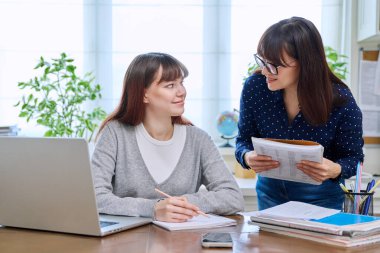 Genç bir öğrenci bilgisayarla masa başında çalışıyor, öğretmen eğitmeni de öğretmenliğe yardım ediyor. Eğitim, öğretim, gençlik kavramı