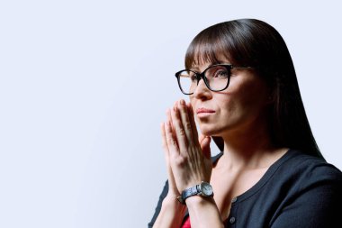 Üzgün, üzgün, gözlüklü, elleri katlanmış, beyaz arka planı kopyalayan olgun bir kadının yakın çekimi. Yalnızlık sorunları, hastalık sorunları, depresyon, dua, akıl sağlığı, orta yaş