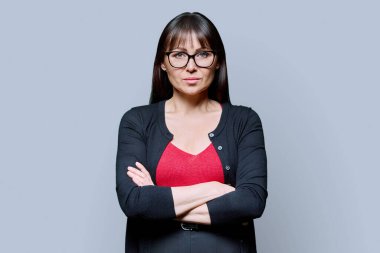 Mavi arka planda çapraz kollu kendinden emin orta yaşlı bir kadının portresi. Gözlüklü, kameraya bakan olgun bir kadın. 40 'ların profesyonel, güzellik sağlık yaşam tarzı iş hizmetleri