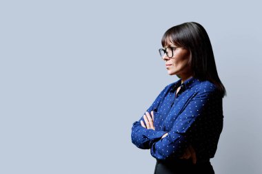 Orta yaşlı, ileriye bakan ciddi bir kadının profil görüntüsü, gri stüdyo arka planı, reklam metni için kopya alanı. Olgun iş, kendine güvenen başarılı kadın. Pazarlama satış hizmetleri, insanlar