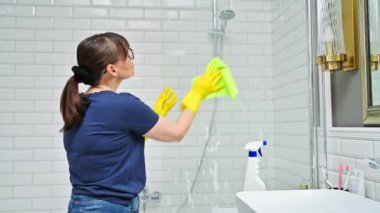 Banyoyu temizleyen kadın, duşta bardağı yıkayan kadın deterjan spreyi ve profesyonel bez parçasıyla. Oda servisi, ev işi, ev temizliği, temizlik hizmeti konsepti.