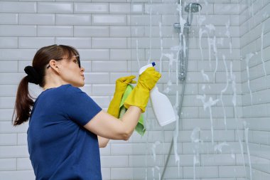 Banyoyu temizleyen kadın, duşta bardağı yıkayan kadın deterjan spreyi ve profesyonel bez parçasıyla. Oda servisi, ev işi, ev temizliği, temizlik hizmeti konsepti.