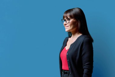 Mavi stüdyo arka planında kendine güvenen olgun bir kadının profil portresi. Orta yaşlı mutlu kadın, reklam metni için mekanı kopyalamaya çalışıyor. İş hizmetleri eğitim sağlığı
