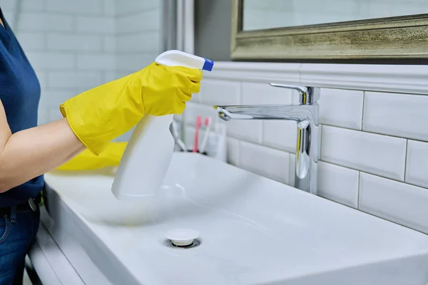 Close-up of cleaning sink with faucet in bathroom, female hands in rubber protective gloves with cleaning detergent and professional rag. Housekeeping housework housecleaning cleaning service concept