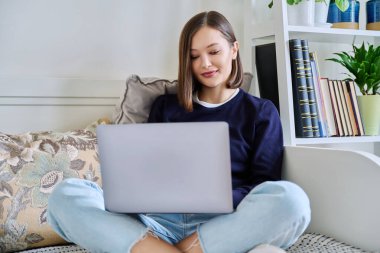 Evdeki koltukta dizüstü bilgisayar kullanan genç bir kadın. İş iletişimi eğitimi için internet çevrimiçi teknolojileri