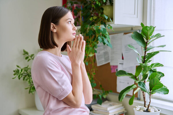 Profile view close-up of young womans face with hands folded in prayer, dreams, memories. Lifestyle, feelings, mental physical health, loneliness, stress, depression, difficulties, youth concept