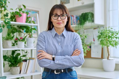 Gözlüklü, kendinden emin orta yaşlı bir kadının portresi. Kolları çapraz giyinmiş, iç mekândaki kameraya bakıyor. 40 'lı yaşlar, yaşam tarzı, sağlık, olgun kadın konsepti