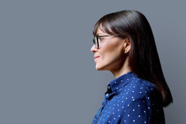 İleri bakan orta yaşlı bir kadının profil görüntüsü, gri stüdyo arka planı, reklam metni için kopya alanı. Olgun iş, kendine güvenen başarılı kadın. Pazarlama satış hizmetleri, insanlar