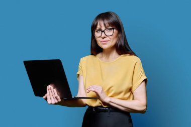 Orta yaşlı iş kadını mavi arka planda dizüstü bilgisayar kullanıyor. Olgun başarılı kadın öğretmen akıl hocası yönetici işçi direktörü. İnternet çevrimiçi teknolojiler, iş, elektronik öğretim