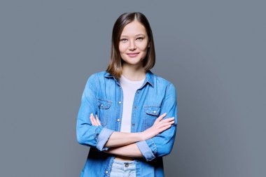 Gri stüdyo arka planında çapraz kollu güzel, kendine güvenen bir kadın. 20 'li yaşlarda, kot giyen ve kameraya bakan çekici bir kadın. Yaşam tarzı, moda güzellik stili, gençlik konsepti
