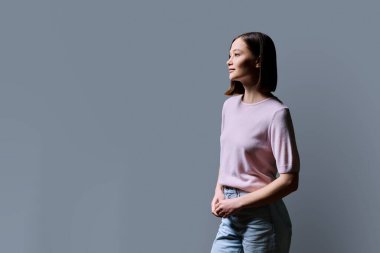 Gri stüdyo arka planında gülümseyen genç bir kadının profil portresi. 20 'li yaşlarda mutlu bir kadın, reklam metni için mekanı kopyalıyor. İş hizmetleri, eğitim, güzellik sağlık hizmetleri