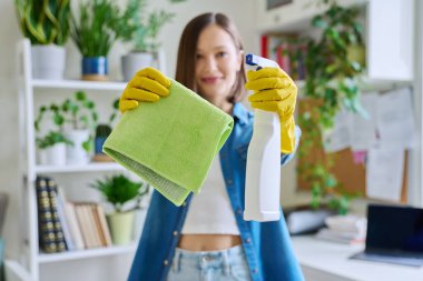 Ev içinde eldiven giyen genç bir kadının ellerinde deterjan spreyiyle temizlik bezine yakın çekim. Rutin ev temizliği, temizlik, ev işi, oda temizliği, ev temizliği, temizlik hizmeti.