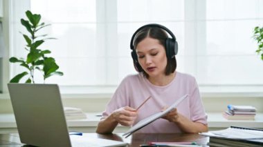Kulaklıklı genç bir üniversite öğrencisi evde oturup sohbet etmek için dizüstü bilgisayarla konuşuyor. İnternet çevrimiçi uzak dersler eğitim eğitimini engelliyor