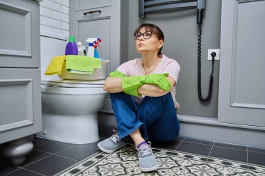 Banyo ve tuvaleti temizledikten sonra yerde oturan yorgun kadın. Rutin ev temizliği, ev hijyeni, ev temizliği, temizlik, ev işi.