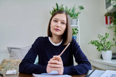 20 'li yaşlarda genç bir kız öğrenci blogger video blogcusunun webcam portresi evde oturmuş kameraya bakıyor. İnternet çevrimiçi webinar görüntülü sohbet konferans teknoloji eğitimi çağrısı