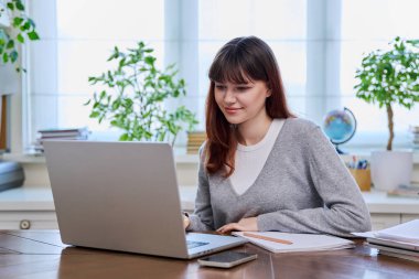 Üniversiteli bir kız masamda dizüstü bilgisayar kullanarak oturuyor, klavyede daktilo kullanıyor, evde. Webinar izleyen genç bir bayan, sınav için hazırlanıyor, uzaktan çalışıyor..