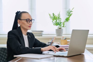 İş kadını ofis masasında dizüstü bilgisayarla çalışıyor. Monitöre bakan 30 'lu yaşlarda ciddi bir kadın. Uzak iş, teknolojiler, internet, öğretim, blog yazma, iş, serbest konsept