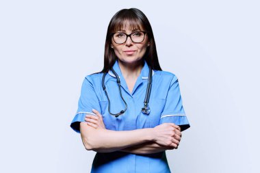 Beyaz stüdyo arka planında steteskopla mavi kollu orta yaşlı kadın hemşire portresi. Tıbbi hizmetler, nhs, sağlık, mesleki yardım, tıbbi bakım kavramı