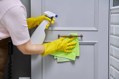 Eldiven temizleme banyosunda yakın plan eller, deterjan spreyli mobilya cephesi ve yumuşak lif bezi. Kadın temizlikçi, ev hanımı, temizlikçi. Oda servisi, ev işi, ev temizliği.