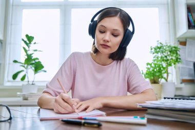 20 'li yaşlarda, kulaklık takan, evinde oturmuş yazı dinleyen genç bir kızın webcam portresi. İnternet çevrimiçi webinar, görüntülü sohbet çağrı konferansı, teknoloji eğitimi