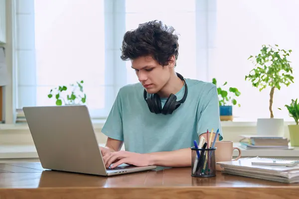 年轻的男大学生坐在家里的办公桌前 用笔记本电脑 20岁的男孩在家里学习 用电脑进行教育 休闲交流 — 图库照片