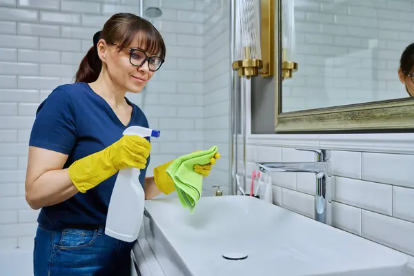 Leende Kvinna Med Rengöringsmedel Spray Tvättlapp Rengöring Badrummet Tvättställ Rutinstädning — Stockfoto