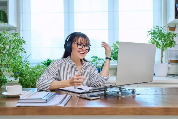 stock image Mature woman in headphones having video conference using laptop computer in home office. Remote virtual meeting, online training, consulting, testing. Work, education, technology, people concept