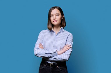 Beyaz mavi arka planda çapraz kollu, kendinden emin, ciddi bir kadın. Gömlekli bir iş kadını, kameraya bakan bir girişimci öğrenci. İş, iş, eğitim, insan kavramı