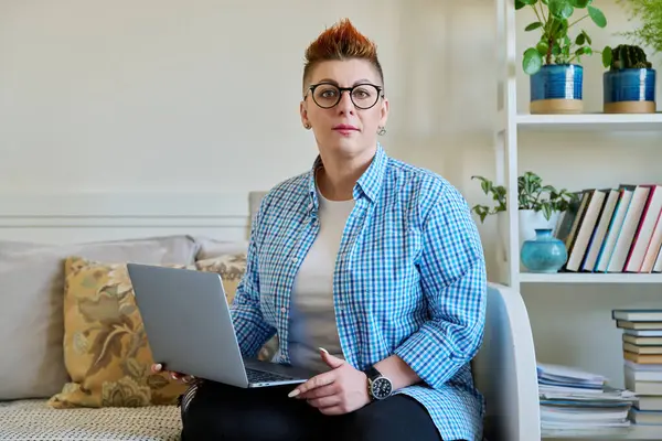 ラップトップを使って自宅でソファーに座り カメラを見ている中年女性 コンピュータで作業するカジュアルな服で赤い髪の真剣な女性 リラックス コミュニケーション — ストック写真