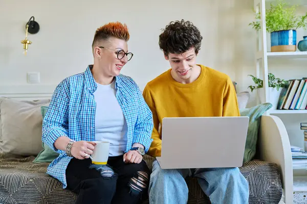 stock image Middle-aged mother and son 19-20 years old sitting together on couch at home looking at laptop screen talking. Lifestyle family communication parenthood tenderness positive relationship two generation