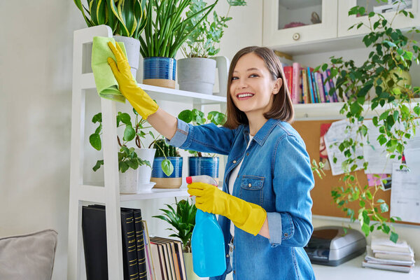 Молодая женщина делает уборку дома, вытирает пыль, надевает перчатки с моющим средством тряпки в интерьере комнаты. Уборка дома, чистота по дому, домашний образ жизни