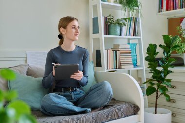 Dijital tabletli genç bir bayan. Stylus evde kanepede otururken resim çiziyor. Teknolojiler, eğlence, yaratıcılık, eğitim, serbest çalışma, yaşam tarzı, gençlik kavramı